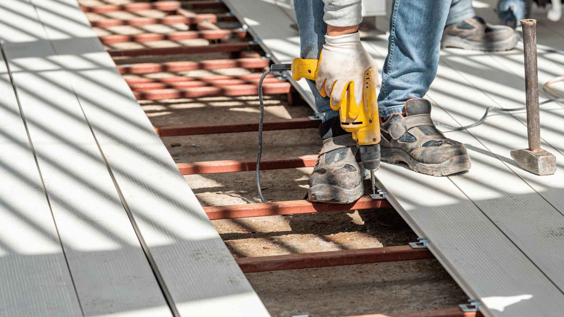 Tradesperson installing composite decking boards onto a metal subframe