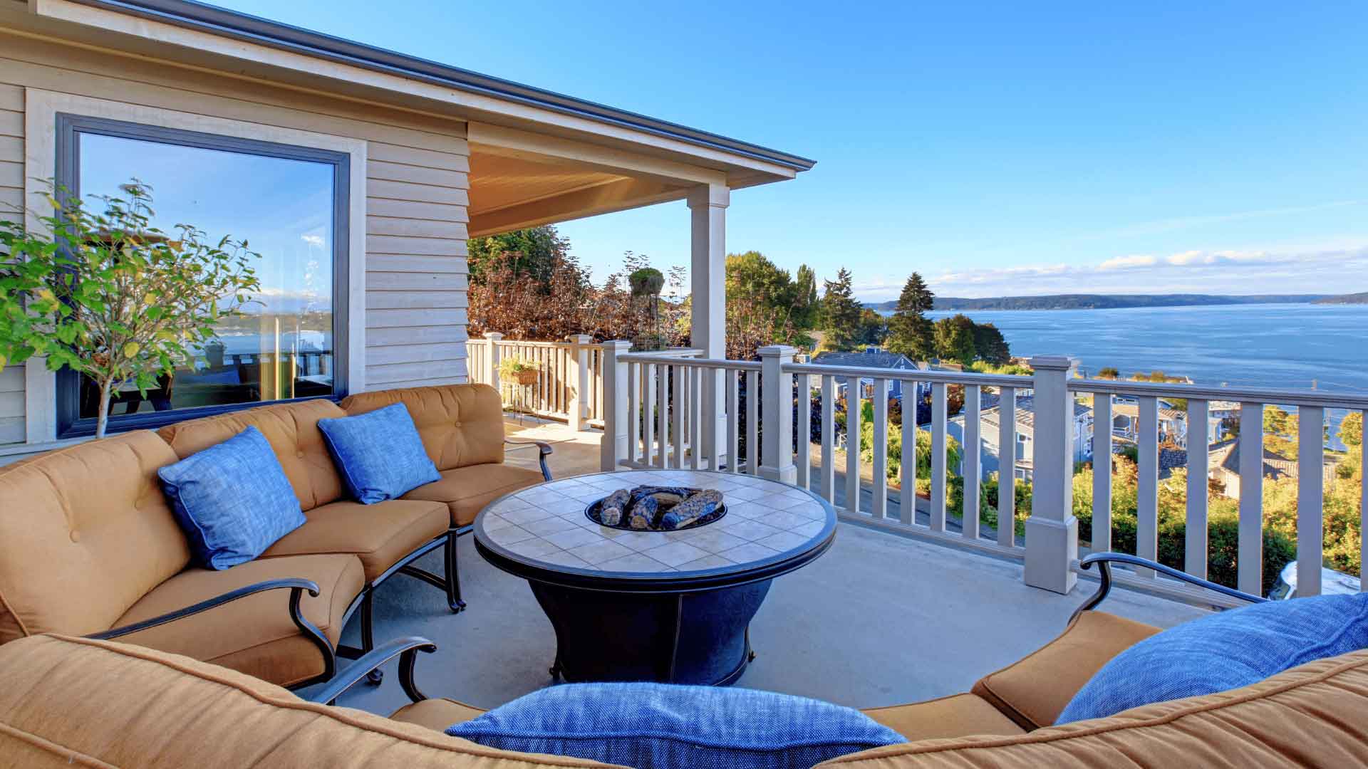 Covered patio with outdoor lounge furniture and fire pit table overlooking the water