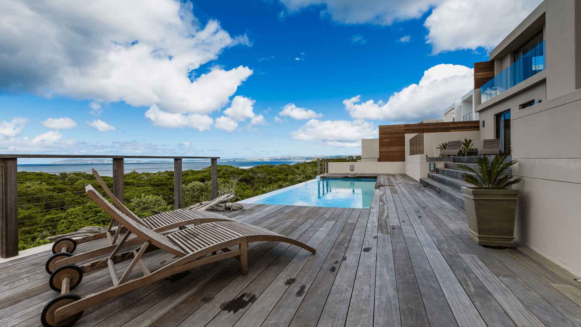 Timber pool deck with a sun lounger beside an infinity pool overlooking the coast