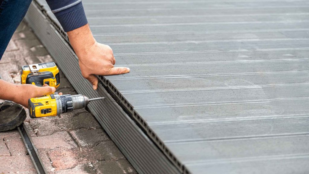 Close-up of hands using a drill to install grey composite decking boards