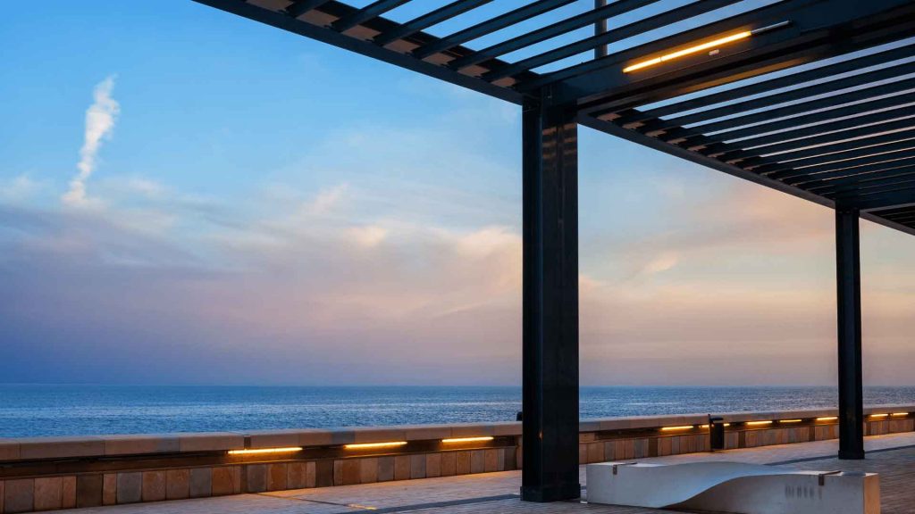 Modern black-framed pergola with integrated lighting overlooking the ocean at dusk
