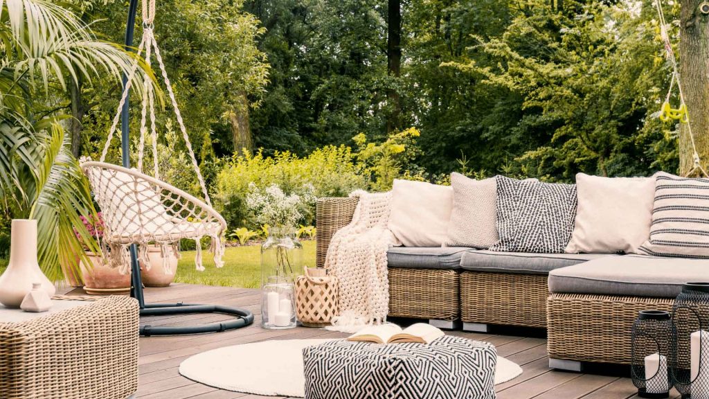 Timber deck with wicker outdoor lounge furniture and a hanging chair, surrounded by garden