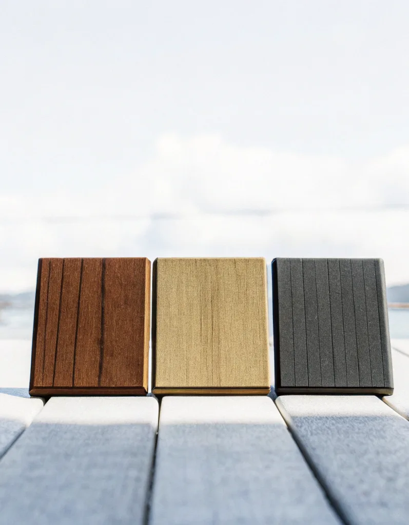 Three composite decking colour samples in dark brown, tan and charcoal grey